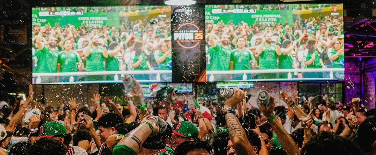 A packed Houston sports bar erupting at a goal, the match live across the screen network we installed